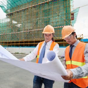 Asian engineers examining plan of building at the construction site