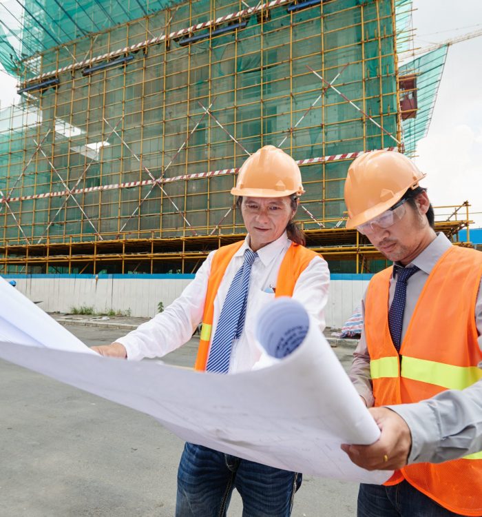 Asian engineers examining plan of building at the construction site